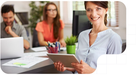 Business services professional smiling and holding a digital tablet in a modern office, while their team collaborates in the background on consulting and analysis tasks.