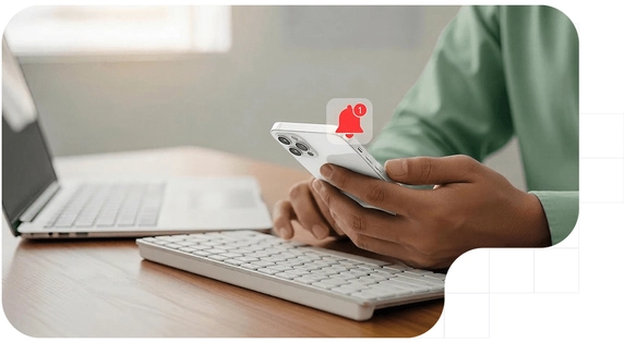 A person receiving a push notification on their phone while working on their computer.